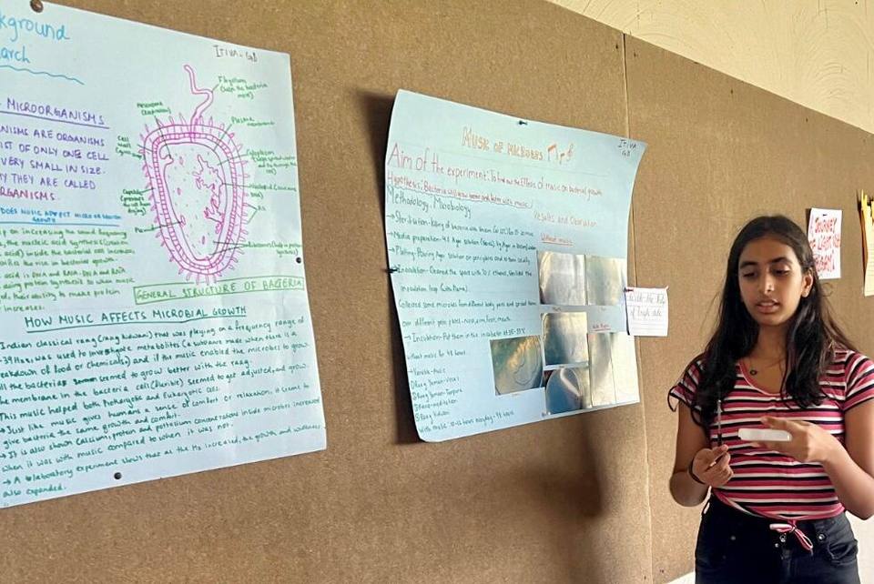 A learner presenting her microbial growth research beside her display boards