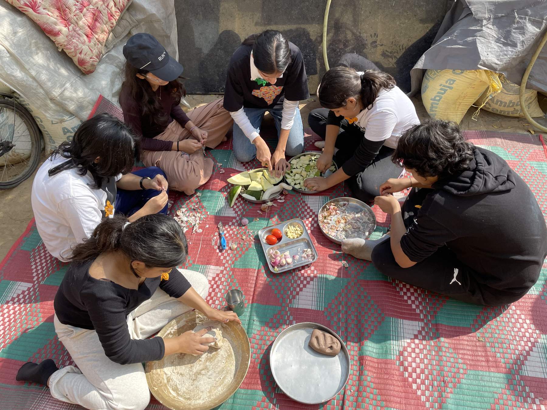 Learners kneading dough and chopping vegetables together on a rug during the Majkhali immersion